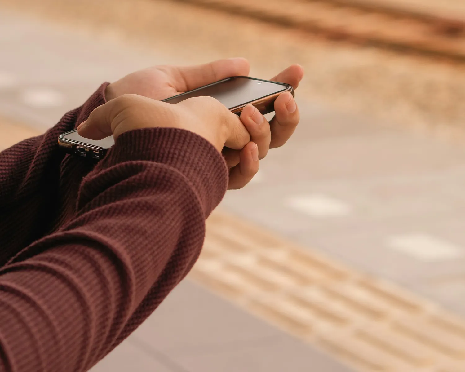 Hands holding a phone on a railway station platform.