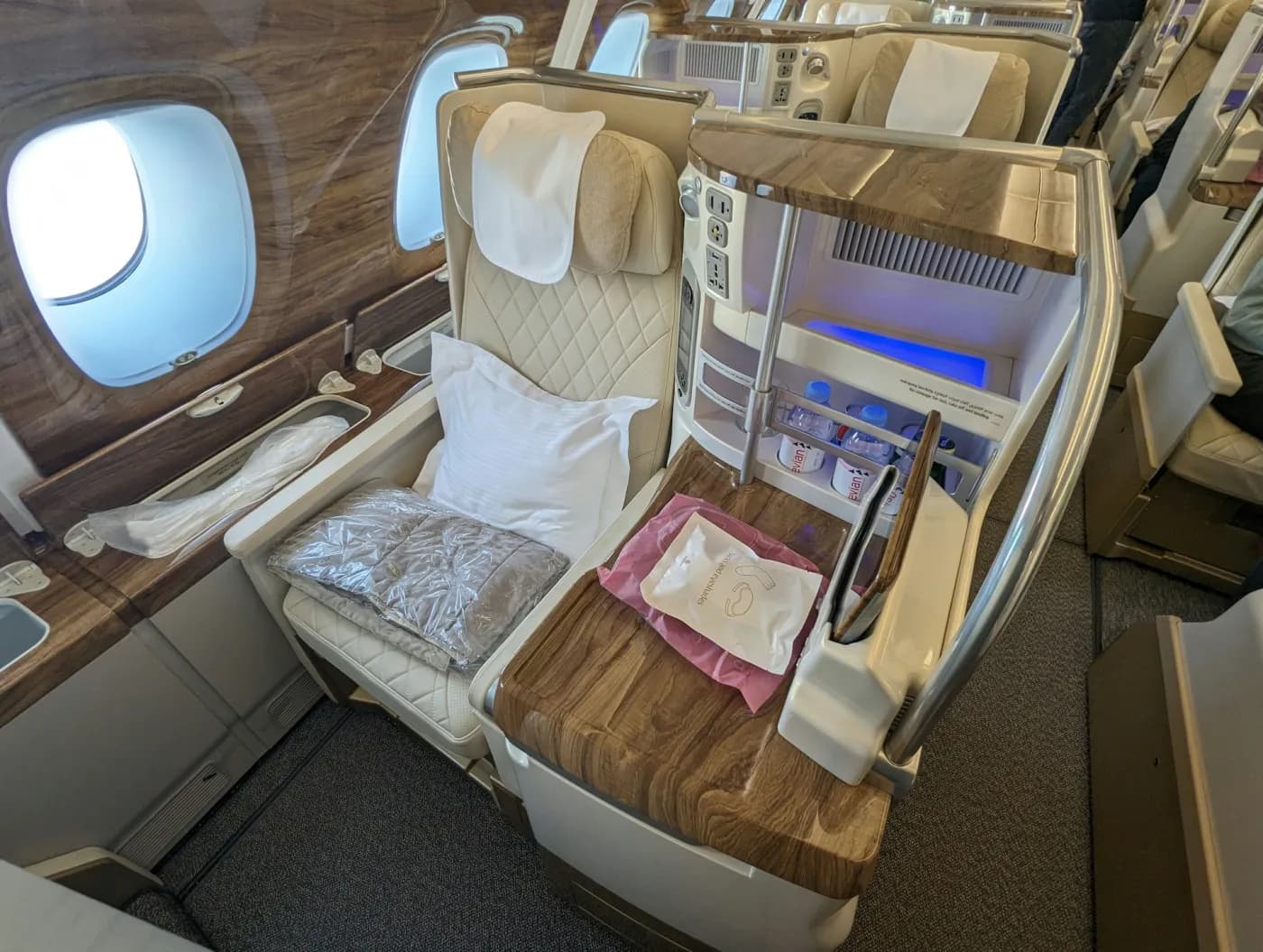 A business class seat with a pillow and a blanket, beside two bright aircraft windows.